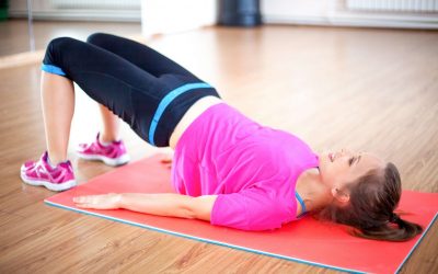 Portrait of happy young Caucasian woman wearing sportswear doing pelvic muscle exercise lying on mat and smiling in gym